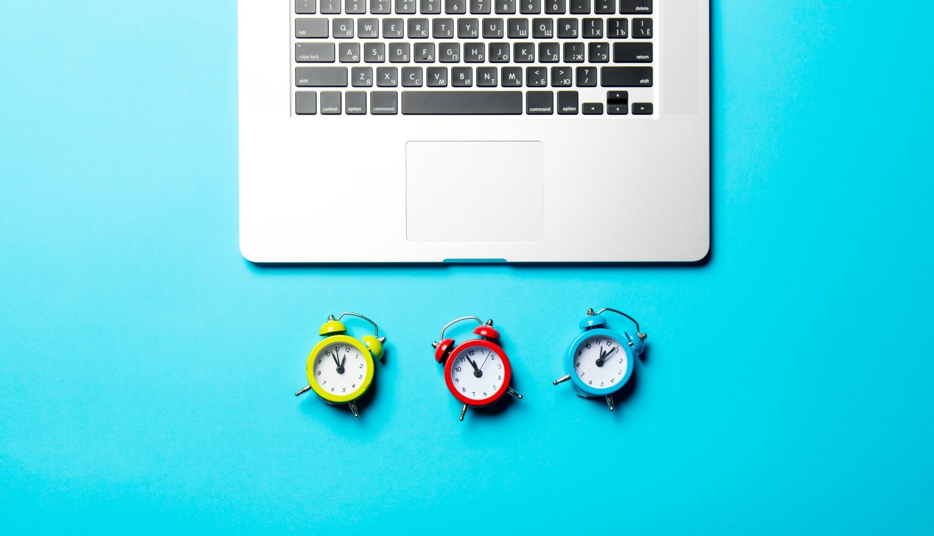 3 small colorful alarm clocks under a laptop
